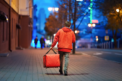 Young delivery person with thermal bag walking at night